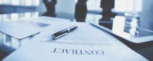 Close-up of business contract with pen at workplace on background of office workers interacting
